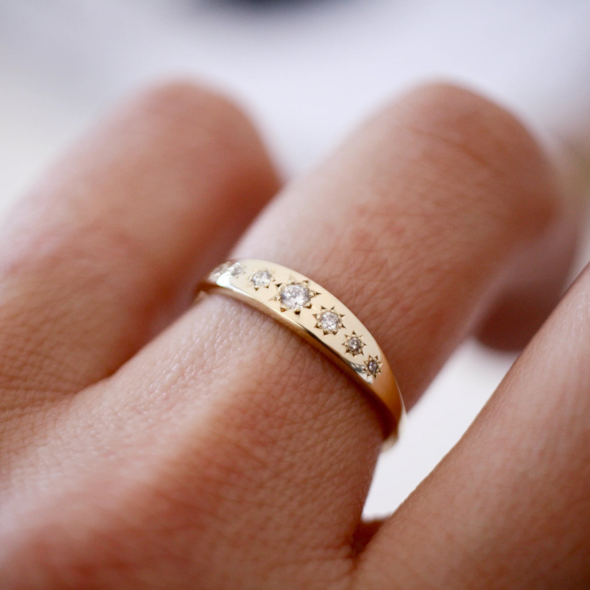 Gold ring with small diamonds on a finger against a blurred background