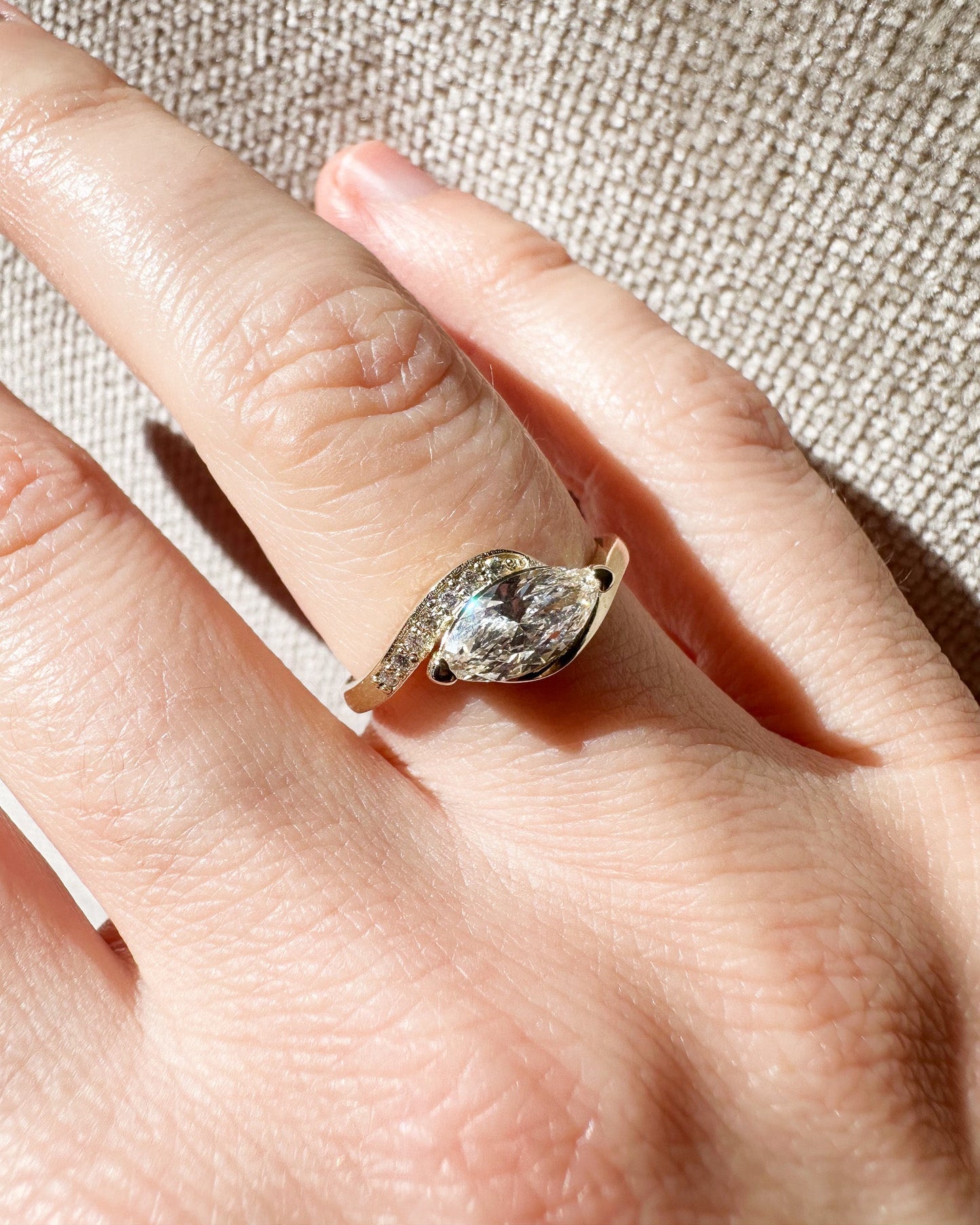 Gold ring with a diamond on a person's finger against a beige fabric background