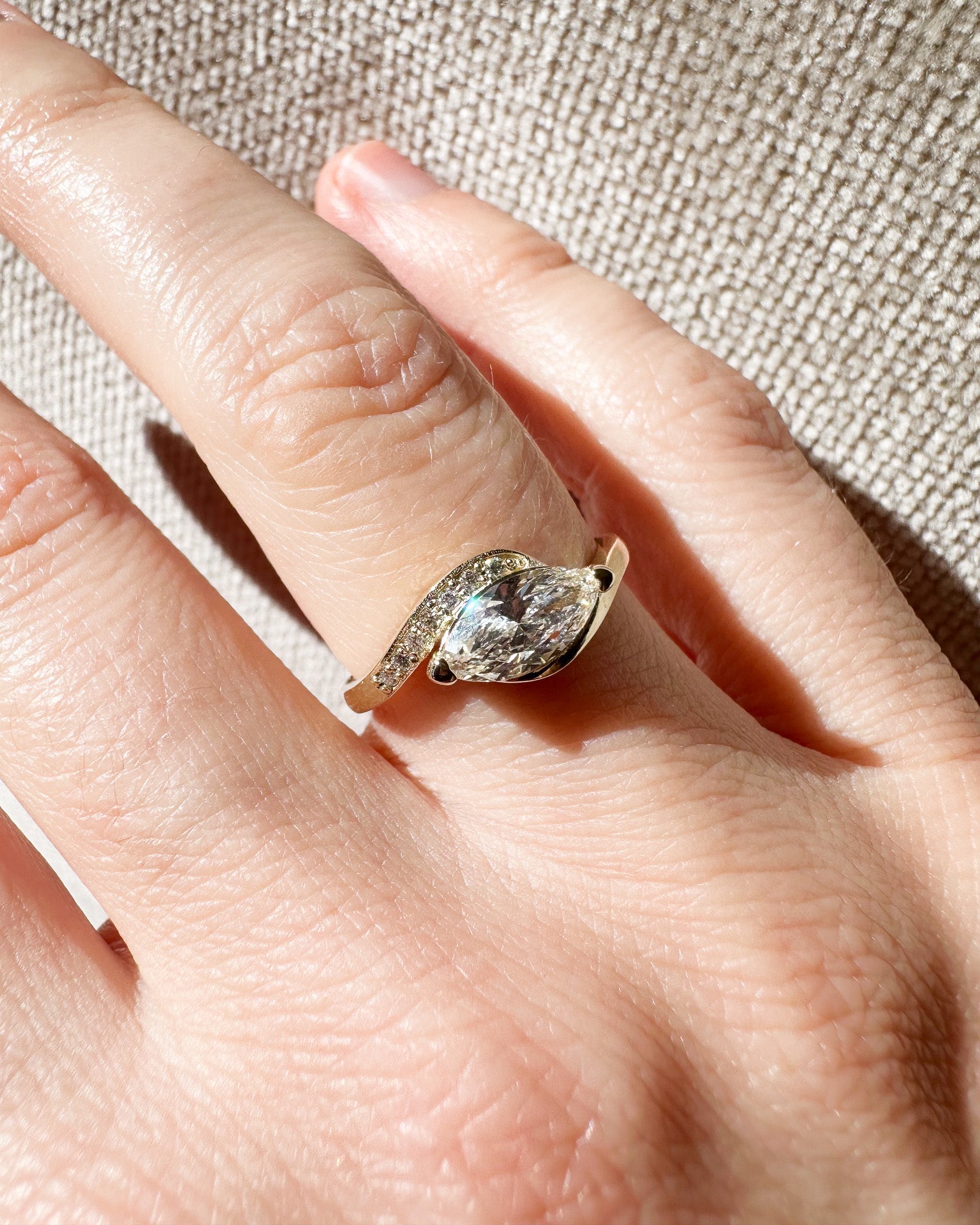Gold ring with a diamond on a person's finger against a beige fabric background
