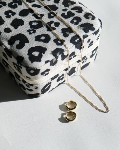 Leopard print pouch with gold chain and gold earrings on a white surface