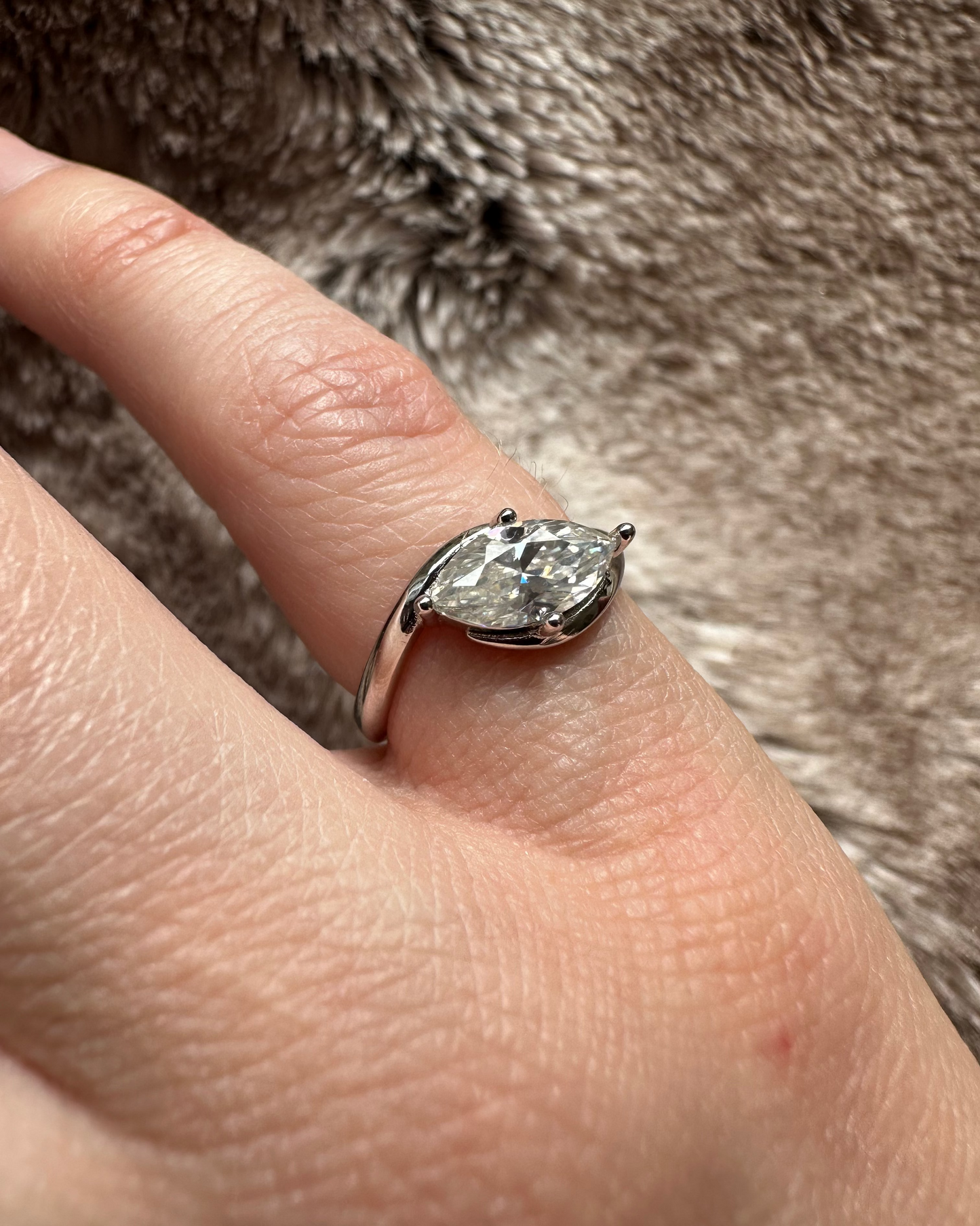 Silver ring with a large diamond on a finger against a fur background