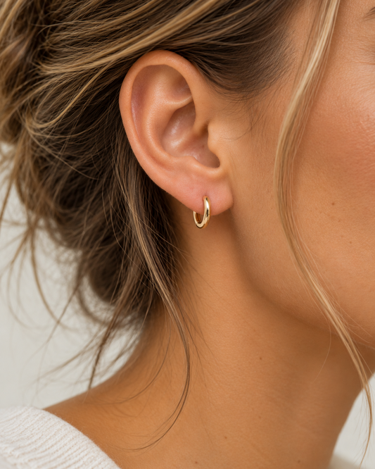 Pair of 9kt solid gold Rounded Huggie Earrings with a polished finish and classic circular design, shown worn on a woman's earlobe.