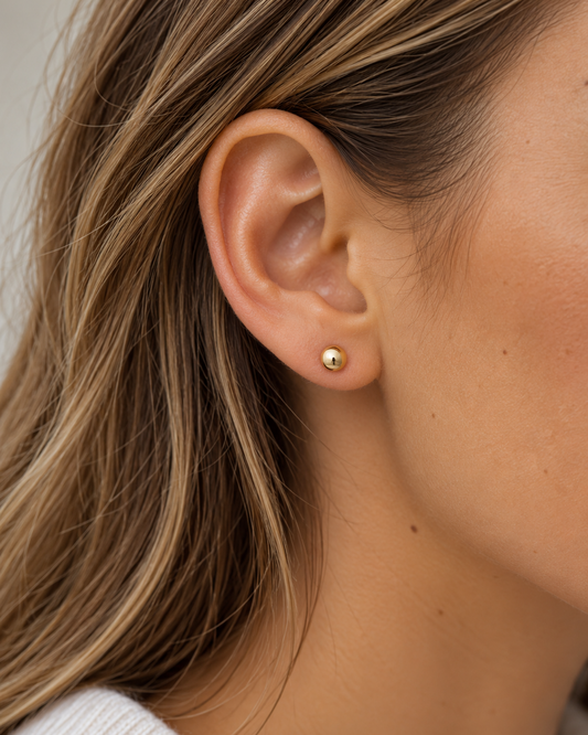 9kt solid gold Dot Stud Earrings featuring a smooth, polished 4.4mm rounded dome design, worn on a woman's earlobe.
