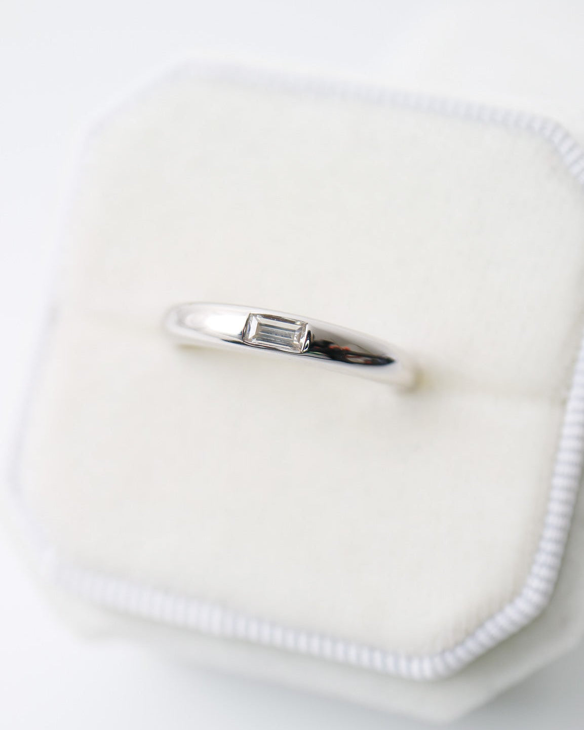 Silver ring on a white cushion with a white background