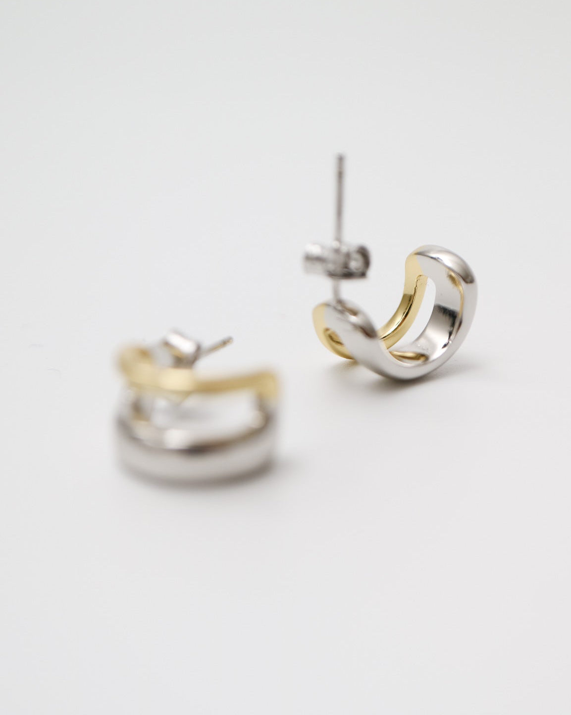 Two small hoop earrings, one gold and one silver, on a light gray background.