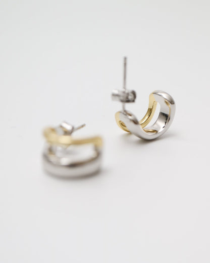 Two small hoop earrings, one gold and one silver, on a light gray background.