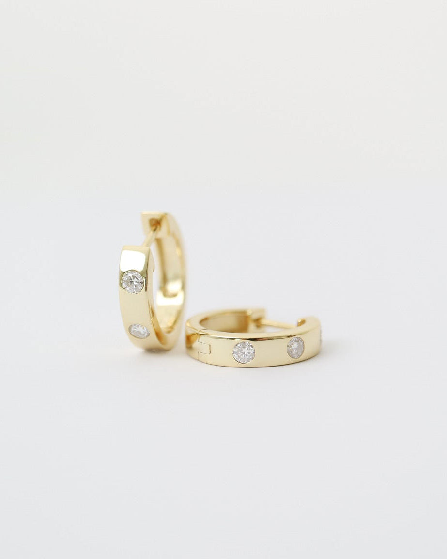 Two gold hoop earrings with small gemstones on a light gray background