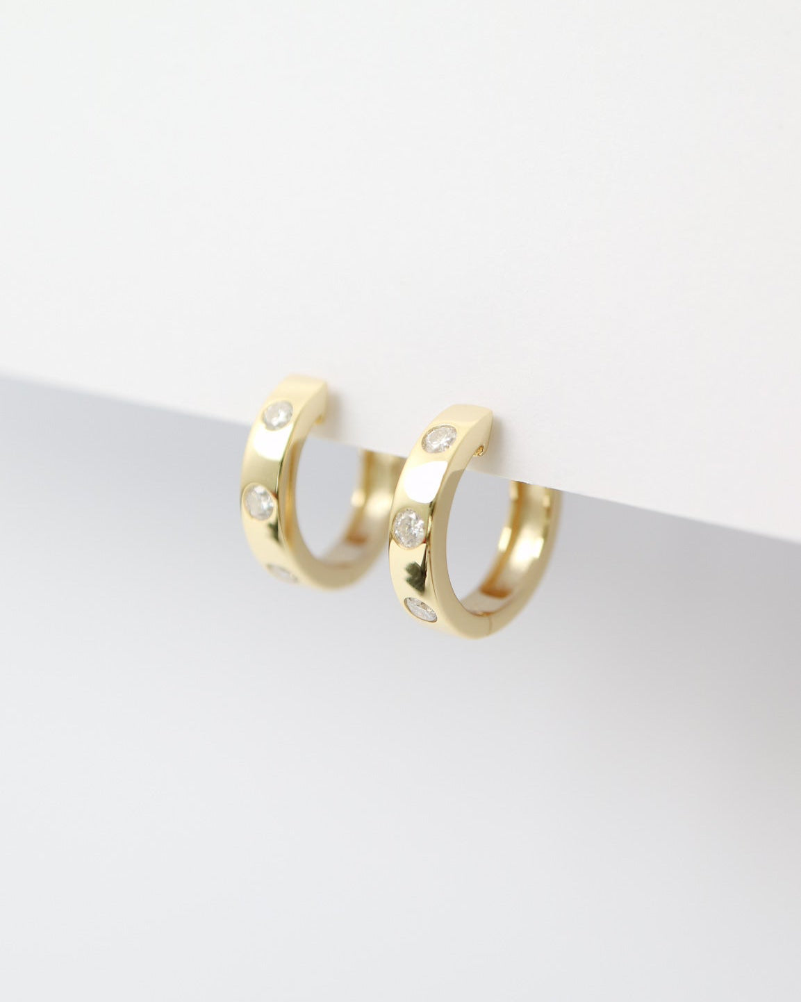 Gold hoop earrings with small diamonds on a light gray background