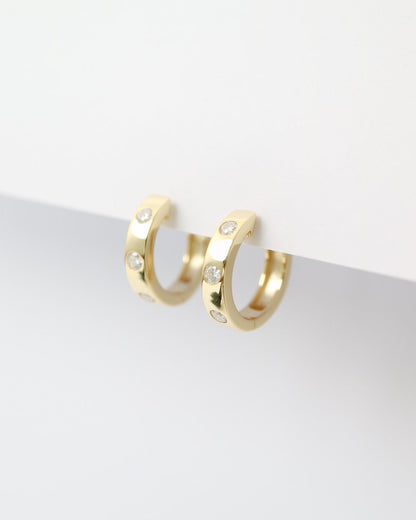 Gold hoop earrings with small diamonds on a light gray background