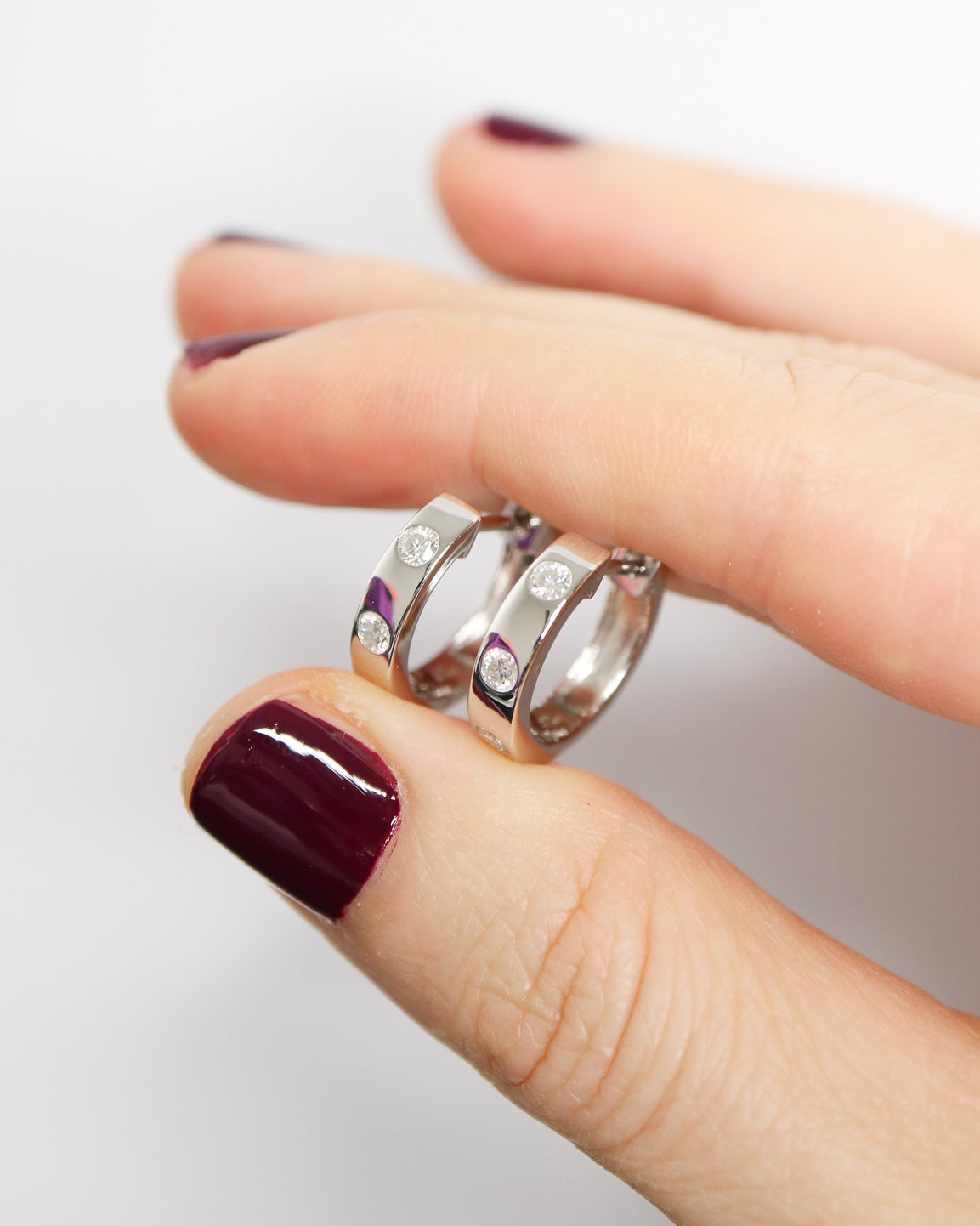 Close-up of a hand wearing three silver rings with gemstones on a light background