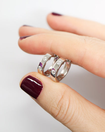 Close-up of a hand wearing three silver rings with gemstones on a light background