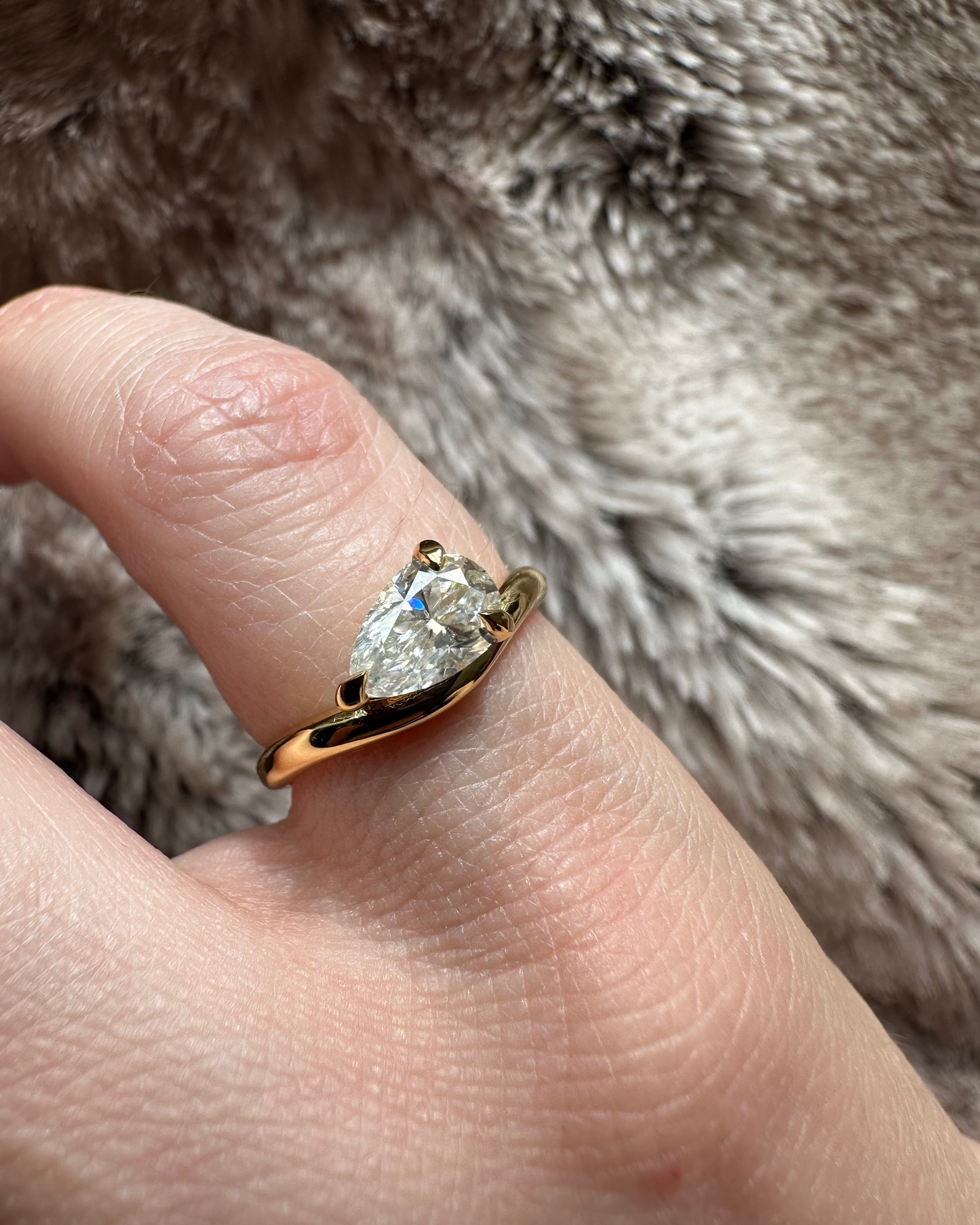 Gold ring with a diamond on a finger against a fur background