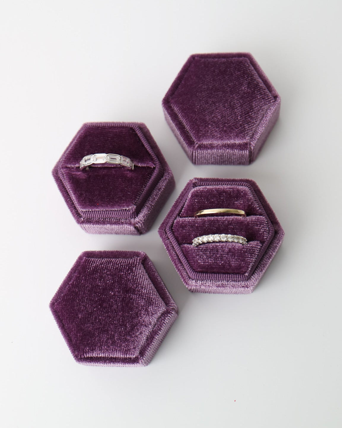 Set of hexagonal purple velvet jewelry boxes with rings inside on a white background