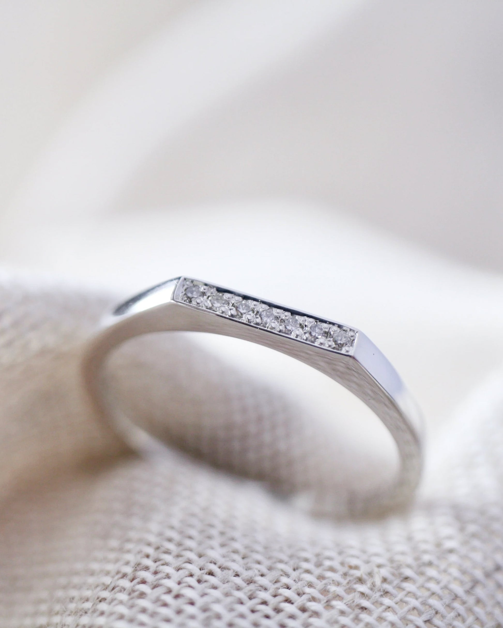 Silver ring with small diamonds on a textured beige surface