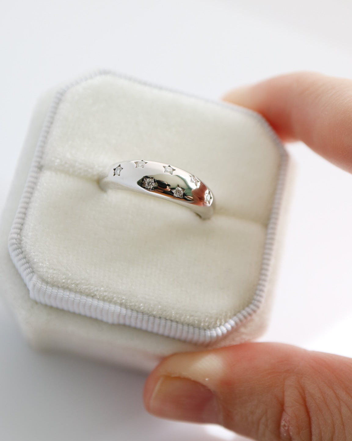 Silver ring on a white jewelry pillow held by a hand against a white background
