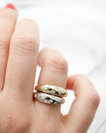 Hand wearing two gold rings with intricate designs on a white background