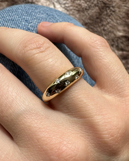 Gold ring with a dark stone on a finger against a textured background