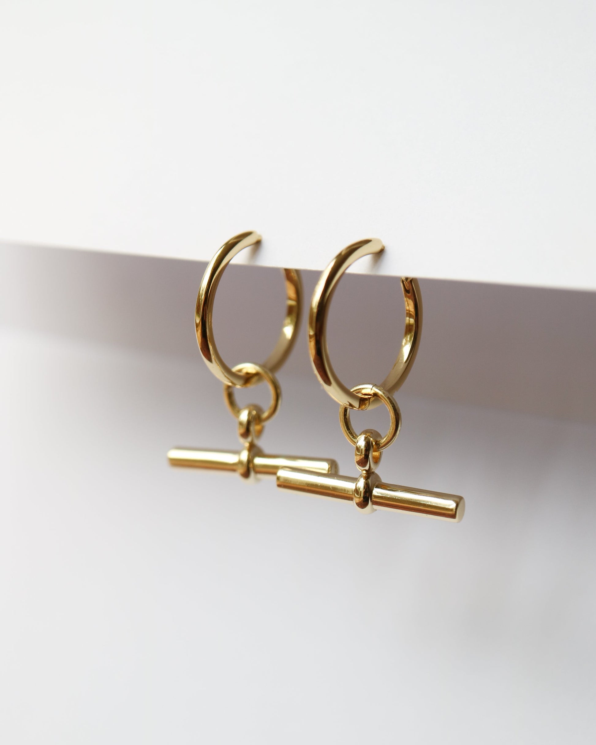 Gold hoop earrings with a small cylindrical charm on a white background