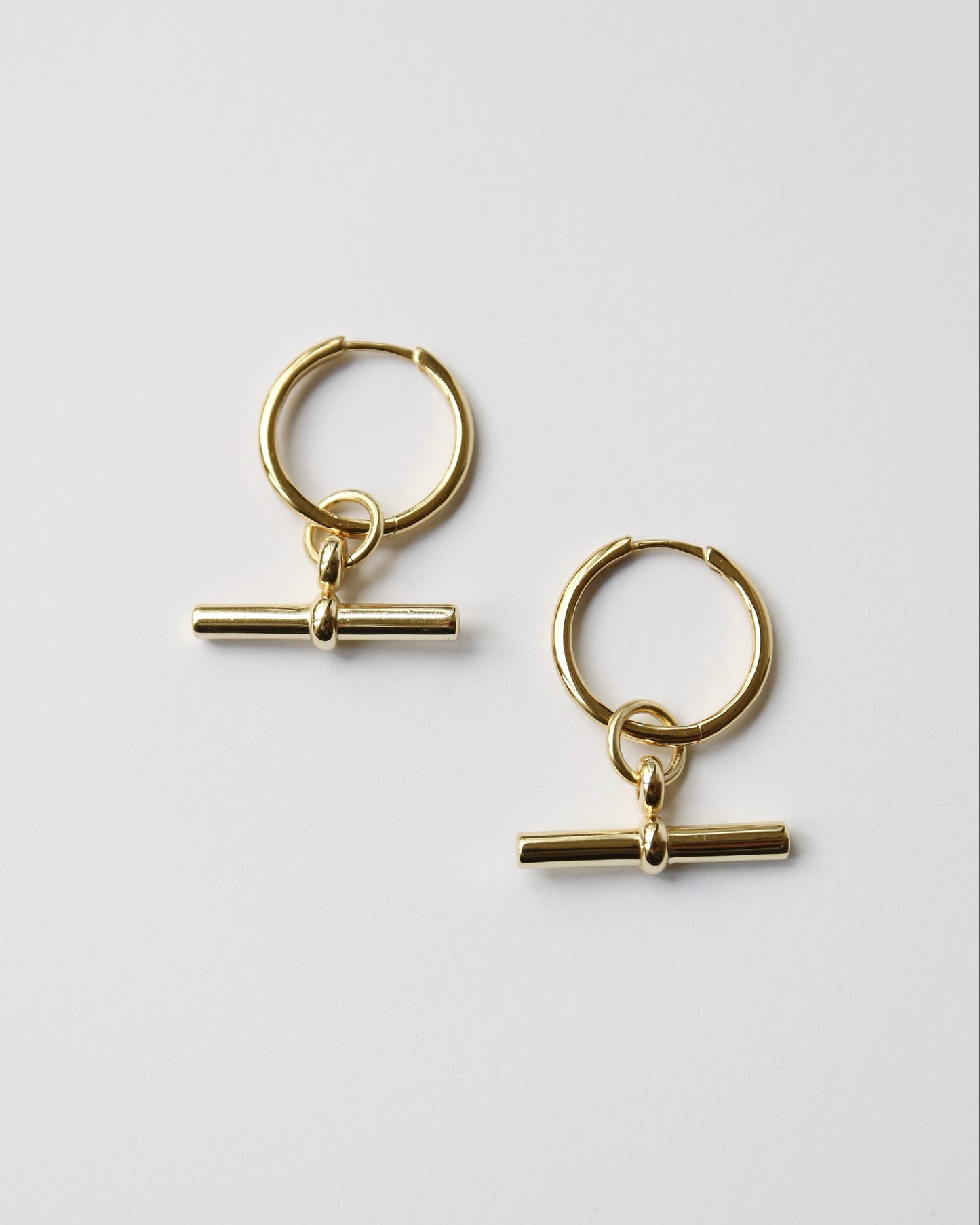 Gold hoop earrings with a bar detail on a light gray background