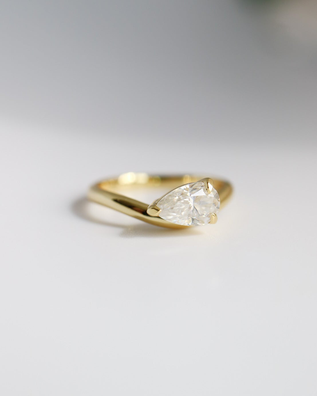Gold ring with a pear-shaped diamond on a light gray background