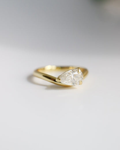 Gold ring with a pear-shaped diamond on a light gray background
