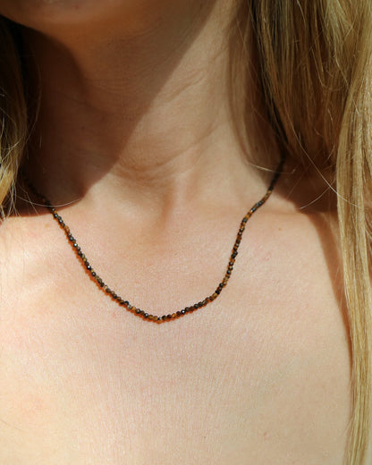 A close-up of a woman's neck and upper chest wearing a delicate beaded necklace with small dark brown and black beads.