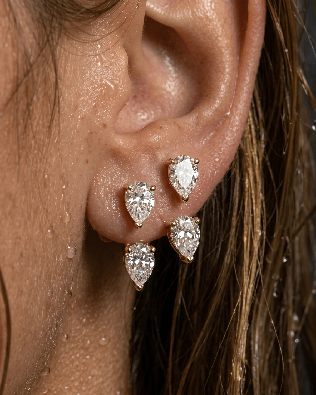 Close-up of an ear wearing gold and diamond teardrop earrings.