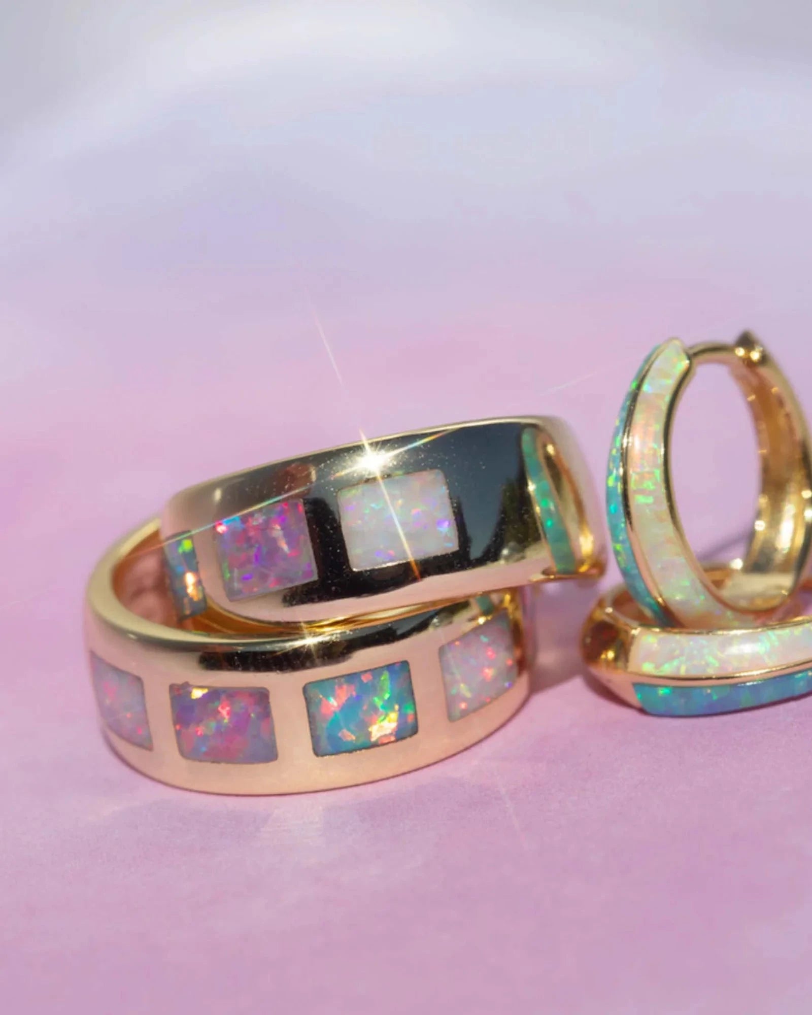 Gold hoop earrings with opal inlay on a pink background