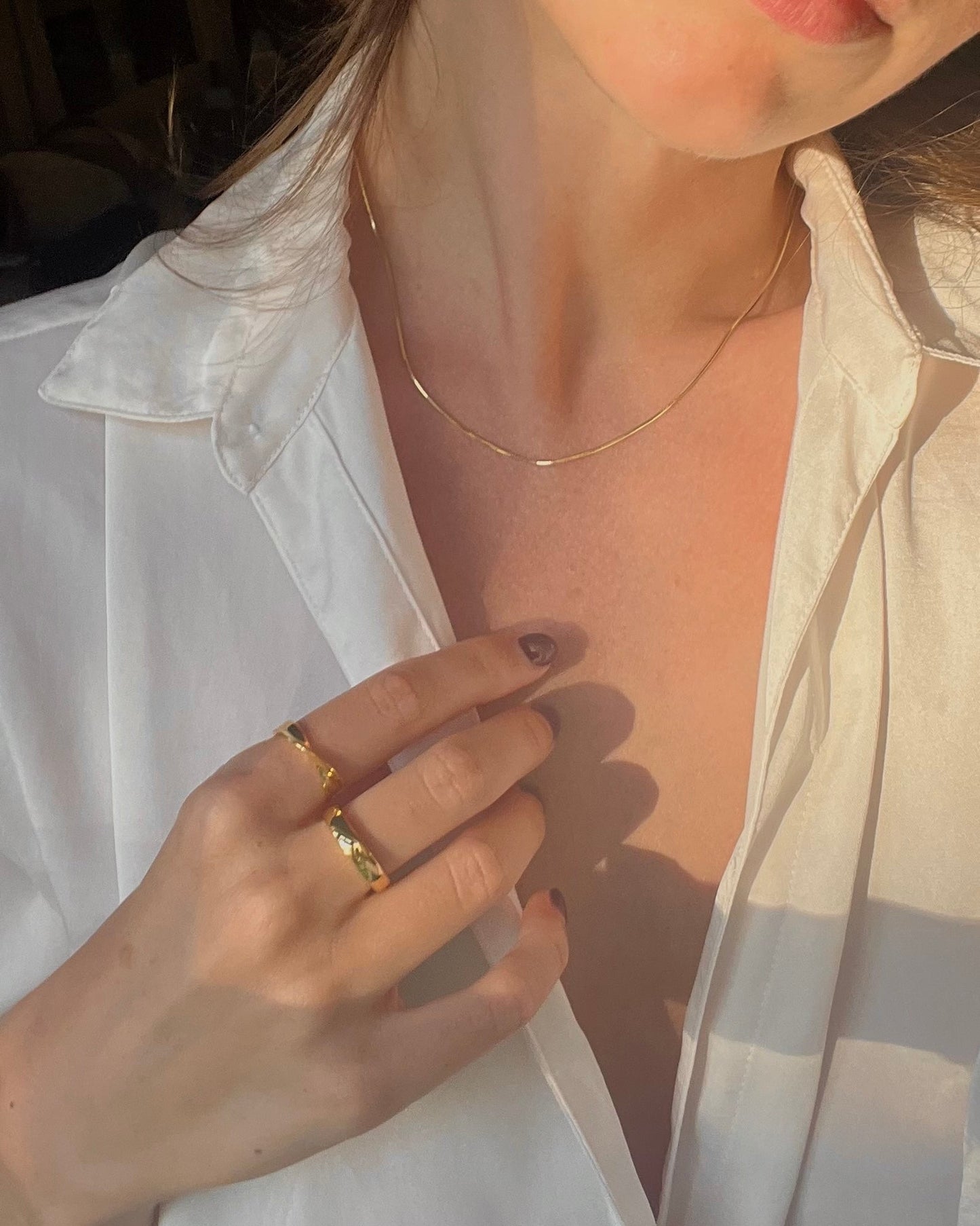 Close-up of a person wearing gold rings and a necklace, with a white shirt.