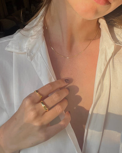 Close-up of a person wearing gold rings and a necklace, with a white shirt.