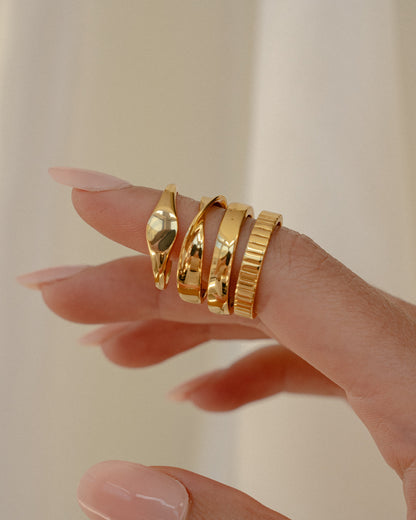 Hand wearing multiple gold rings on a neutral background