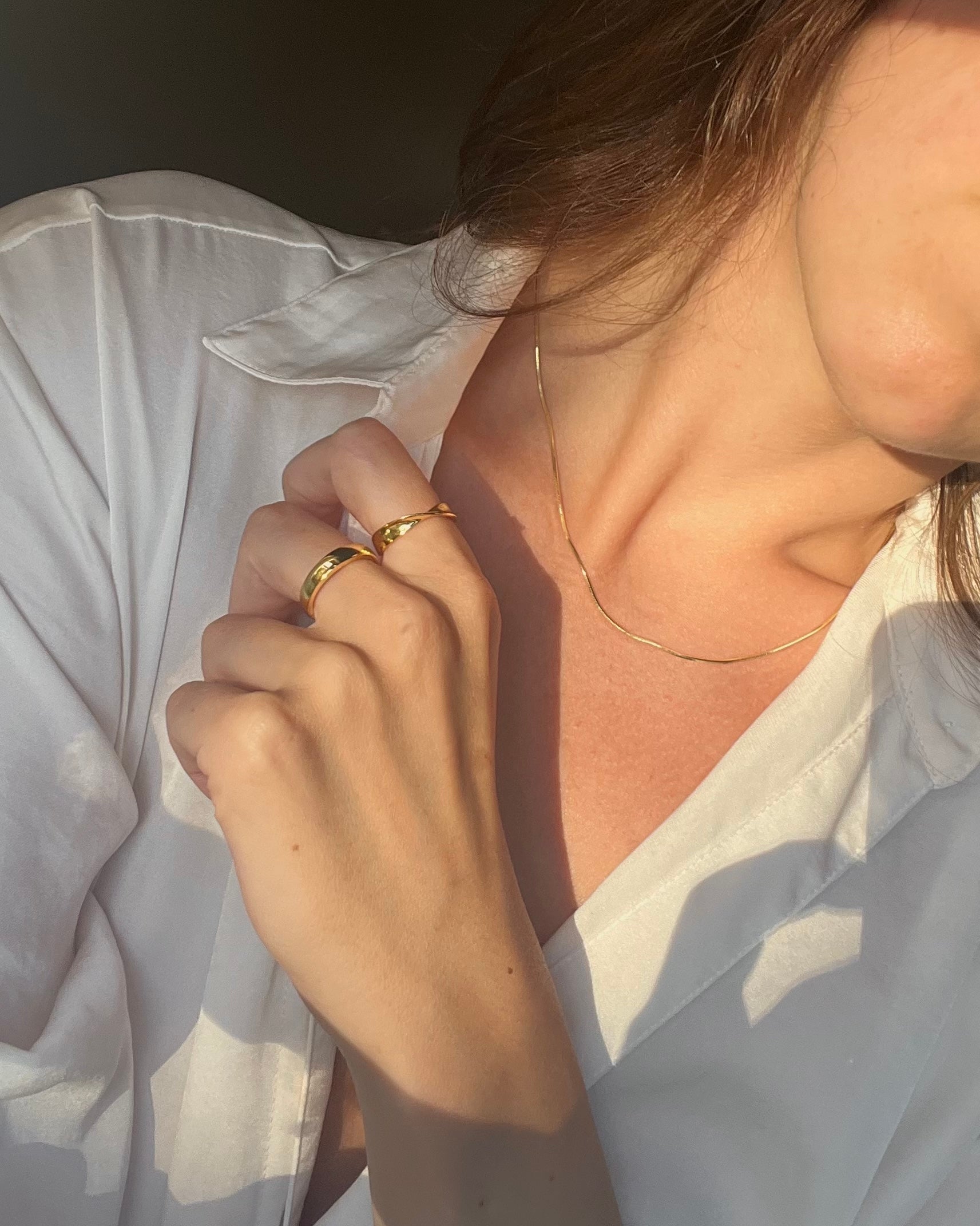 Person wearing a gold ring and gold necklace with a soft focus background