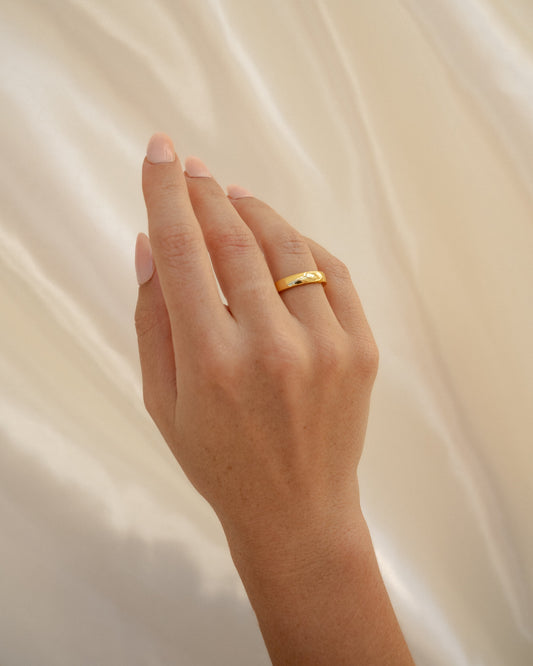 Hand wearing a gold ring on a soft beige background