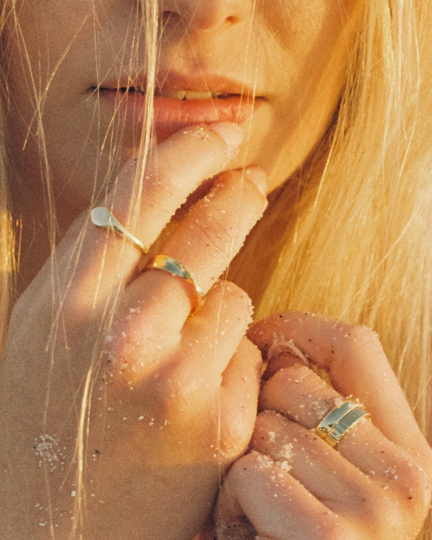 Close-up of a person's face with blonde hair and gold rings on fingers, with a warm glow.