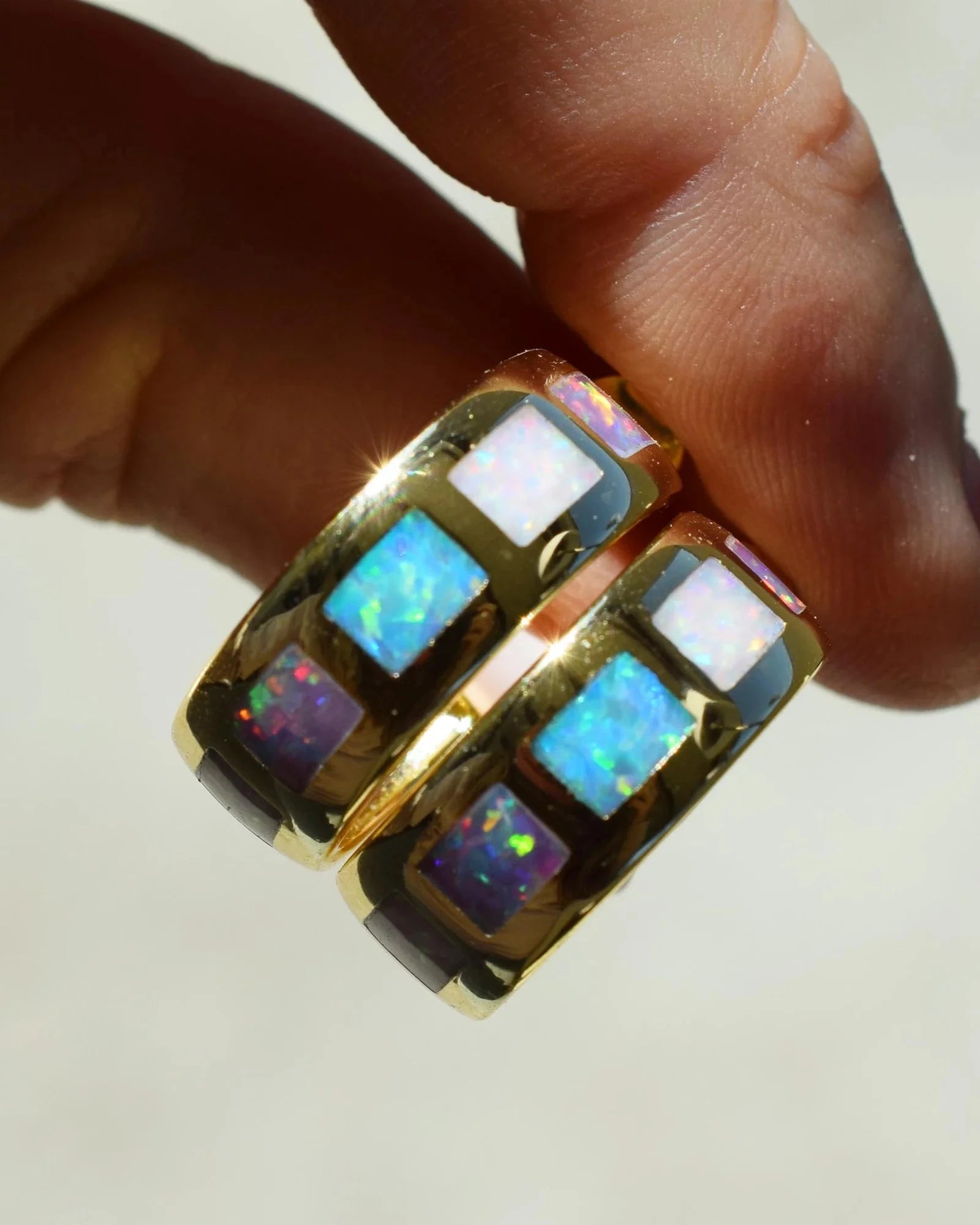 Gold ring with opal stones held by a hand on a light background