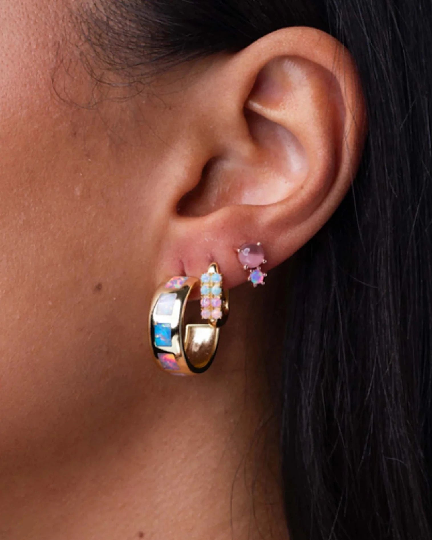 Close-up of an ear wearing gold hoop earrings with colorful gemstones.