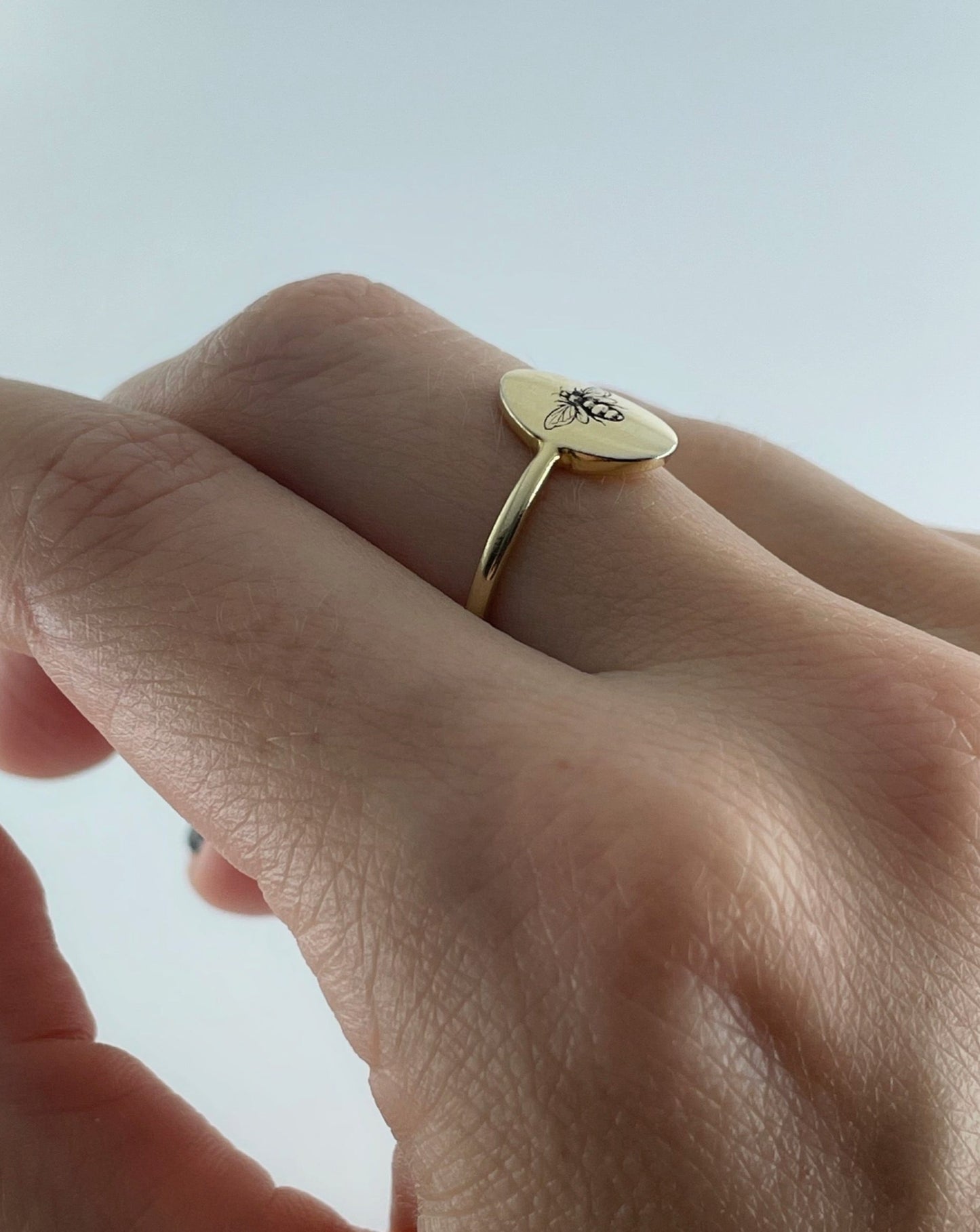 9ct oval ring with bee engraving, shown from the side of a human hand