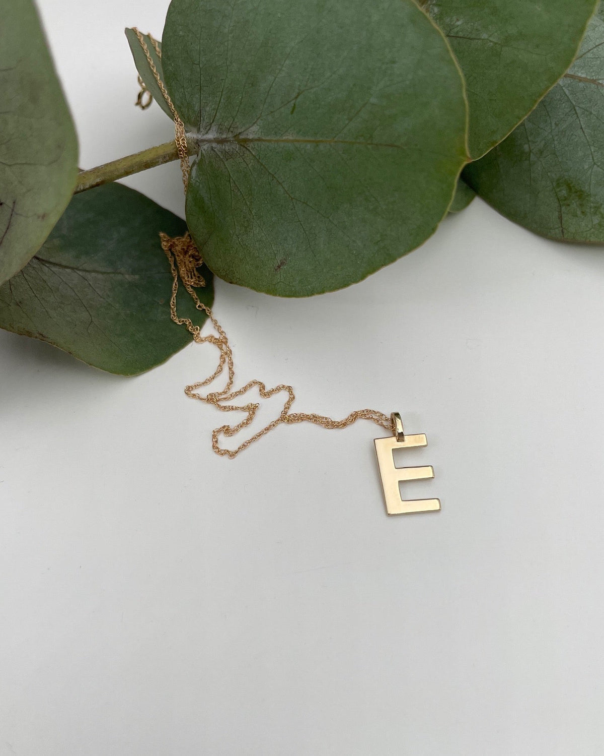 Gold E Initial on gold chain, shown on white with eucalyptus  