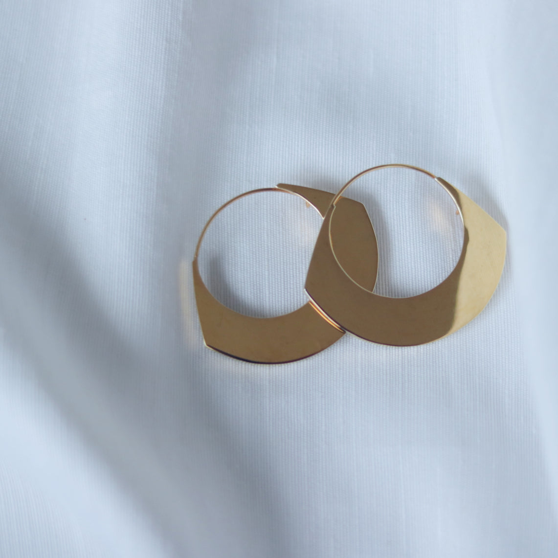 Yellow gold plated statement earrings on white linen background